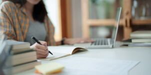 Frau sitzt mit Lernunterlagen und Laptop am Tisch und schreibt