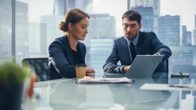 Frau und Mann in Business Outfits sitzen am Tisch mit Laptop und diskutieren