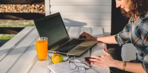 Frau sitzt mit Laptop, Handy und Unterlagen draußen an einem Tisch